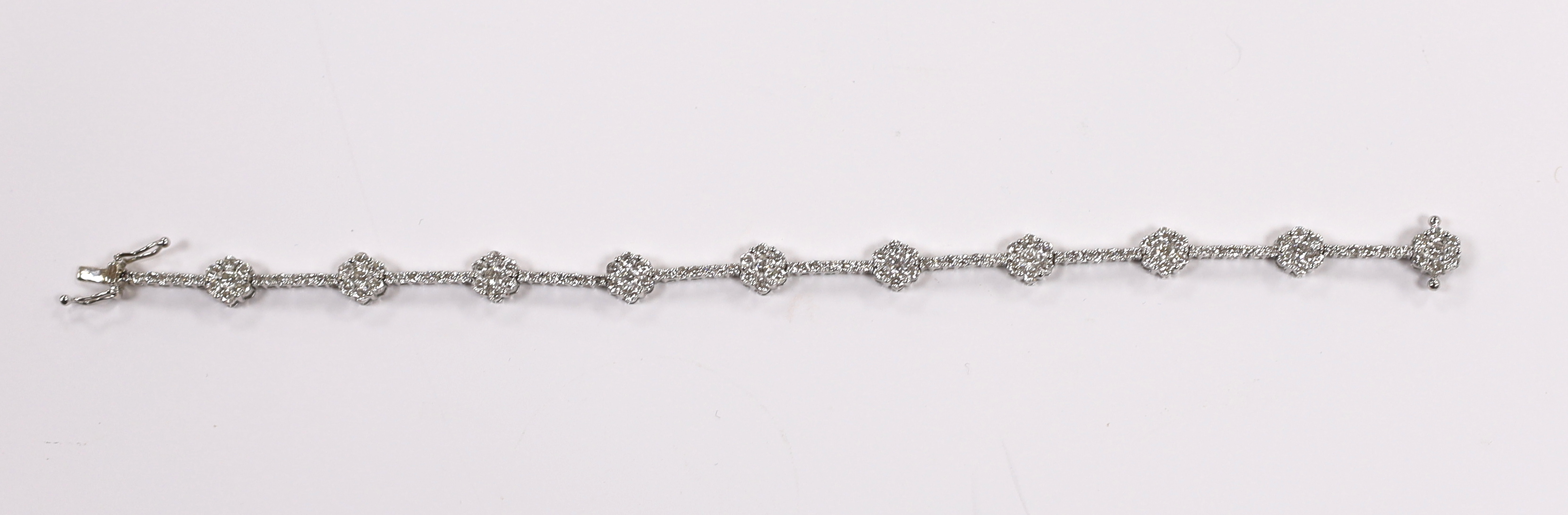 A modern 18k white metal and diamond cluster set flower head line bracelet, 17.5cm, gross weight 8.4 grams.